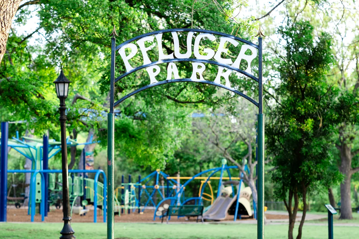 Entrance sign to Pfluger Park with playground in the background.